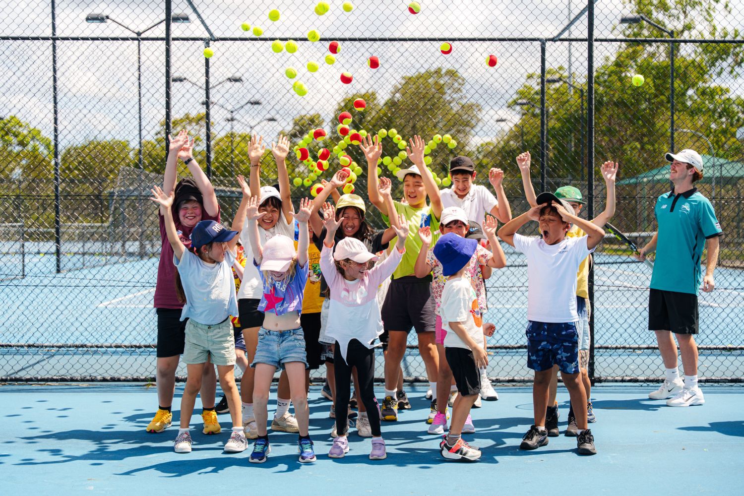 Juniors celebrating on court as tennis balls are thrown in the air